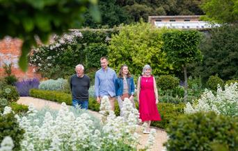 Two men and two woman walk around Holkham's Walled Garden, surrounded by white flowers.