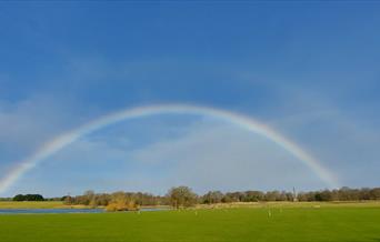 The image shows Holkham Park with the lake and monument. A rainbow appears over the Park.