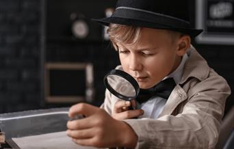 A boy in a black hat and bow tie looking through a magnifying glass.