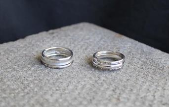 Two stacks of silver rings with different textured sitting on a light grey material.