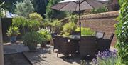 A photo of the patio at aylsham Windmill viewed from the front threshold. Sunny, with verdant pot plants, glasstop table, chairs and sunshade