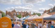 Crowds of people attending Holt Sunday Market. Gazebos line a closed road, creating a street carnival atmosphere on a sunny and bright day.