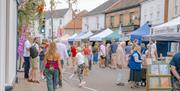 Crowds of people attending Holt Sunday Market. Gazebos line a closed road on a sunny and bright day.