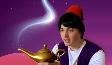 A young boy with black hair and wearing a red fez, Aladdin, holds a golden lamp
