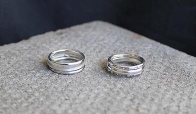 Two stacks of silver rings with different textured sitting on a light grey material.