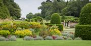 Formal gardens with colourful flowers, grass lawns and yew hedge topiary.