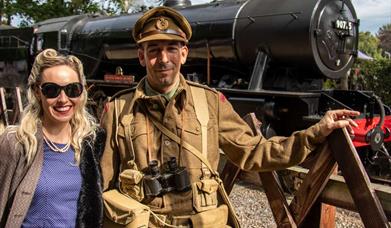 Couple pose in vintage fashions next to steam train at Holt Station