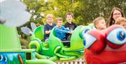 Three children sat on a green fun fair ride.