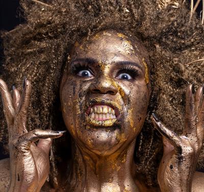 Desiree Burch covered in gold paint pulling a somewhat manic expression.