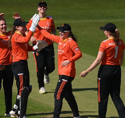 A photo of the women's cricket team ont he pitch. They are hi-5ing one another.