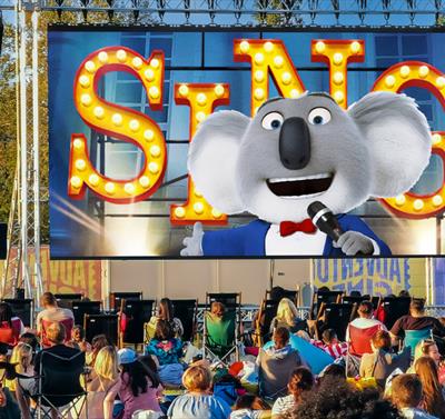 Photo of an outdoor cinema screen showing a still from SING.