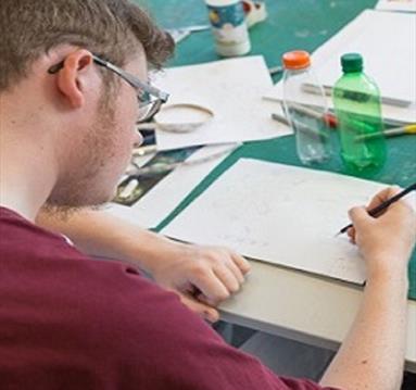 Photo of a student writing in a notebook, taken from behind his shoulder.