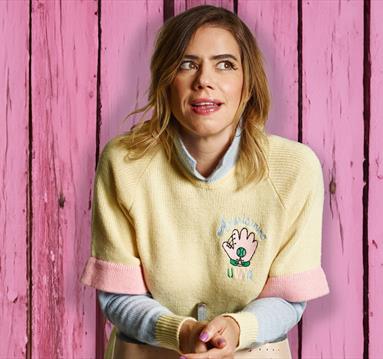 Photo of Lou Sanders in front of a wooden backdrop which is painted pink