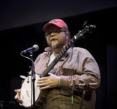 Riley Baugus speaks, banjo in hand, to the audience between numbers