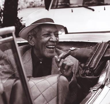 Edgar Macías Quintet, smiling, smoking cigar in a covertible car.
