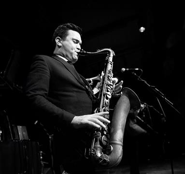 Black and white photo of a member of the Brandon Allen Quartet playing a saxaphone mid-performance