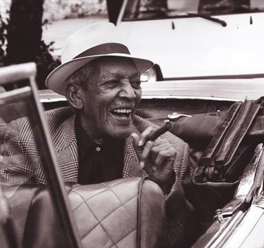 Edgar Macías smiling in back seat of open top car smoking a cigar