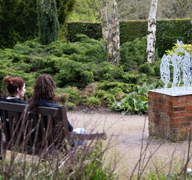 Photo of one of the art installations. Two people are sitting on a bench opposite, looking at it.