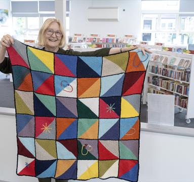 Photo of a woman holding up a blanket made from crochet squared