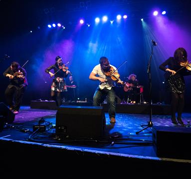 Band playing violins on a blue lit stage.