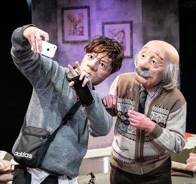 Photo of the stage show showing two puppets: one of a young boy, the other of an old man