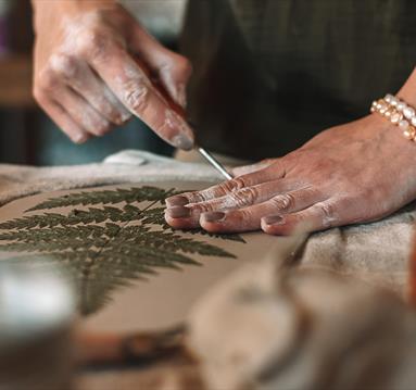 Photo of a person engaged in an activity on a tabletop. They appear to be undertaking a craft with clay and leaves,