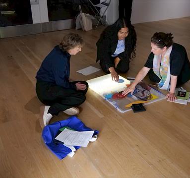 Three people seated on the floor around an art sketchbook