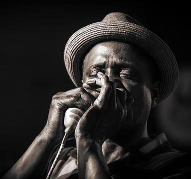 Black and white photo of a performer playing a harmonica into a microphone