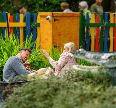 Photo og a family on a water ride, with a toy aligator int he foreground and colourful fences in the background. They are laughing and happy.