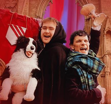Two characters dressed as Byron and a monk stand back to back in raucous laughter, beckoning the camera with wide smiles.
