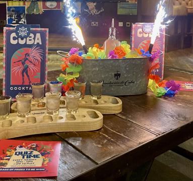 Photo of a bar table with cocktails in wooden trays, drinks menus and sparklers