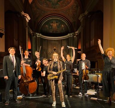 Image shows a band on stage holding various instruments.