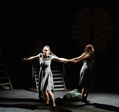 A photo of two performers on a bare stage.