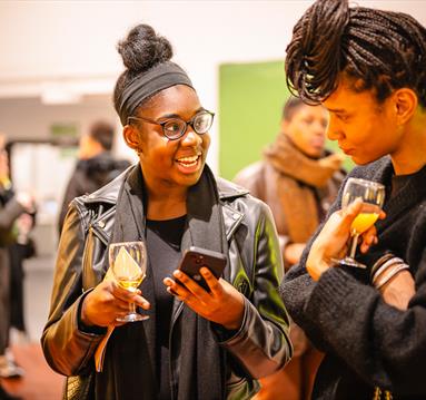 Photo of visitors at an exhibition launch party holding drinks and talking