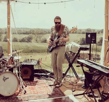 Shot of Mucky slide playing on stage in a gazebo looking out over rolling countryside