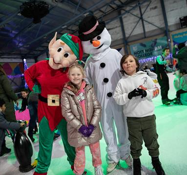 Photo of kids skatingb with costumed characters dressed as Santa's Elf and a snowman