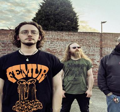 Four band members stand in front of a brick wall