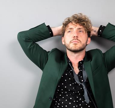 Comedian Seann Walsh, wearing a spotted shirt, black tie and dark green jacket