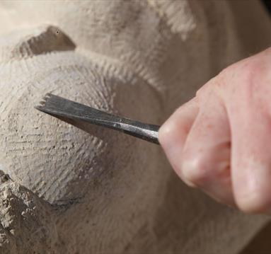 Image shows a mans hand carving a stone
