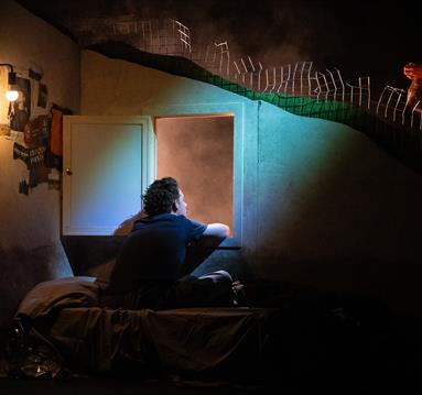 Image shows a young boy sitting alone in a dark room with an open door and a blue light shining in.