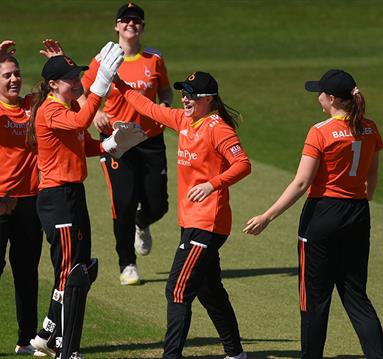 A photo of the women's cricket team ont he pitch. They are hi-5ing one another.