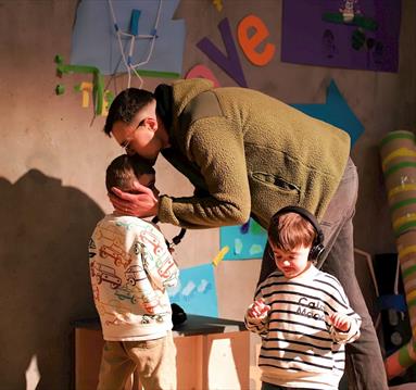 A father beding down to kiss his child, who is engaged in a play session