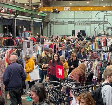 Crowds gathered around rails of discounted clothing at an indoor flea market