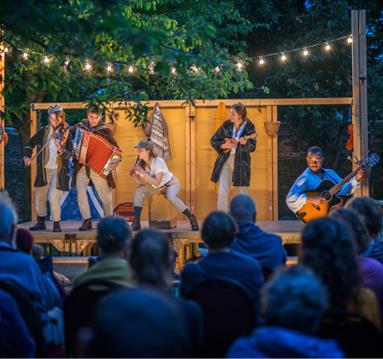 Photo of an outdoor theatre in the evening with performers lit up on stage