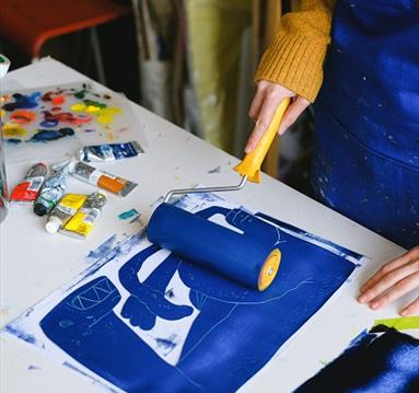 The image shows someone rolling blue paint on some paper using a paint roller.