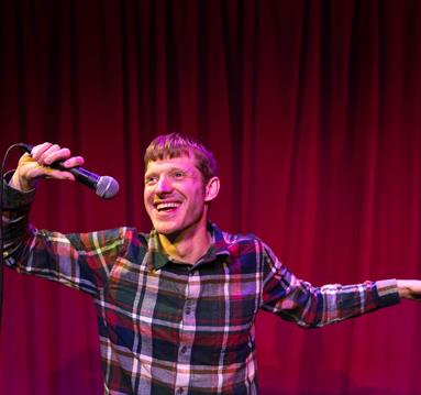 The image shows David Eagle stood on stage holding a microphone. 