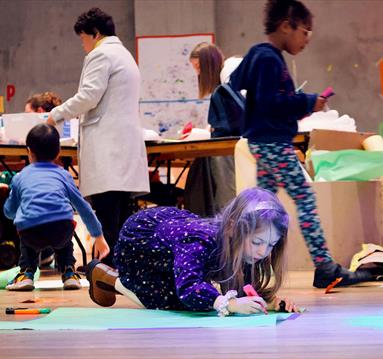 Photo of children at Nottingham Contemporary. A young girl is seen in the foreground colouring on the floor