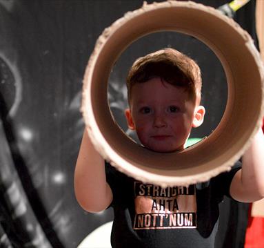 Young child looking through a large cardboard tube