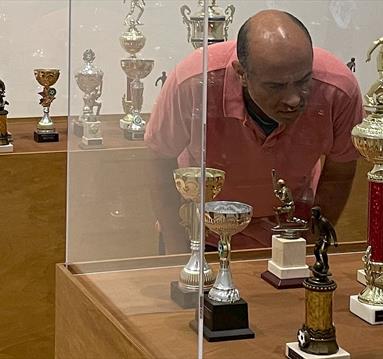 Photo of a man looking at trophies behind a glass exhibition