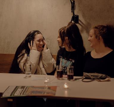 Phot of women sitting at a table, looking at eachother.